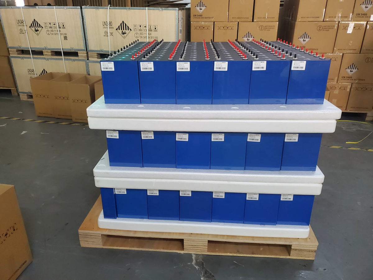 Real warehouse photo showing prismatic LiFePO4 cells separated by protective spacers beside packed cartons during a staged procurement review