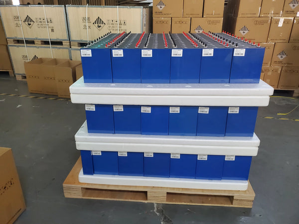 Real warehouse photo showing prismatic LiFePO4 cells separated by protective spacers beside packed cartons during a staged procurement review